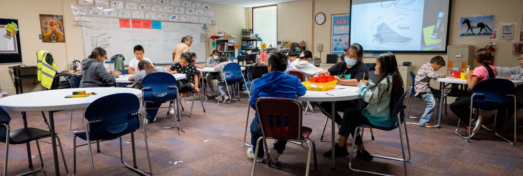 A busy classroom filled with children sitting at tables, engaged in learning and working on various activities together.