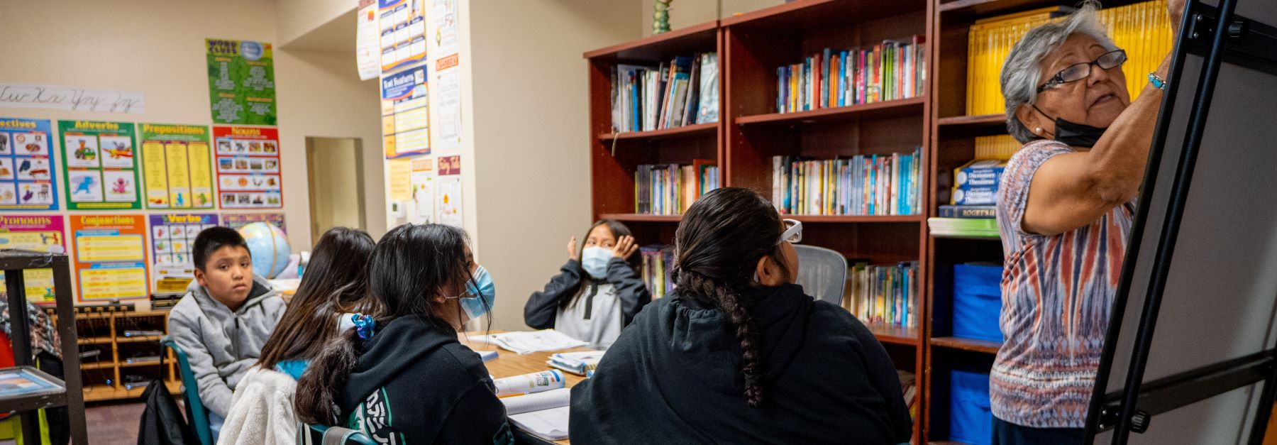 A teacher stands in front of a classroom, engaging students who are attentively listening and taking notes.